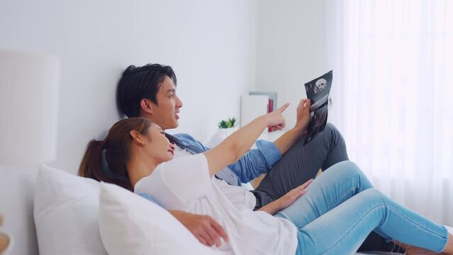 Asian young couple watching ultrasound pregnancy test photo in bedroom. 