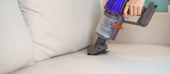 Woman cleaning Sofa with cordless Vacuum cleaner. Housewife using wireless Vacuum for big cleaning...