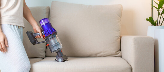 Woman cleaning Sofa with cordless Vacuum cleaner. Housewife using wireless Vacuum for big cleaning home. Housework, Housecleaning, Housekeeping, Removes dust, Domestic hygiene and daily routine