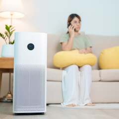 Air Purifier with woman relax and use smartphone on sofa. Purification system for filter and cleaning dust PM2.5 HEPA and virus in home. Allergy, Pure air, health, Wellness lifestyle and Air Pollution