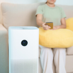 Woman turn on Air Purifier in living room by smartphone application. Purification system for filter and cleaning dust PM2.5 HEPA and virus. Allergy, Pure air, health lifestyle and Air Pollution