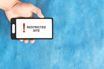 Hand holding a mobile phone with Restricted Site and Website Blocked and Access Denied message...