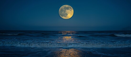 Full moon ascending above the sea as powerful waves break on the shore in the foreground