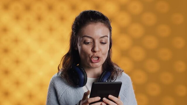 Voice actor reading ebook in entertaining manner in front of audience, portraying character, studio background. Woman reenacting digital novel for spectators, reading from tablet screen, camera A