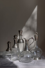 A collection of five clear glass decanters with varying designs and stoppers sits on a draped...
