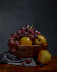 Apples, grapes, and lemon in a rustic wooden bowl placed on a linen tablecloth. Close-up view showcasing the vibrant colors and fresh textures of the fruits against the neutral background. Ideal for f