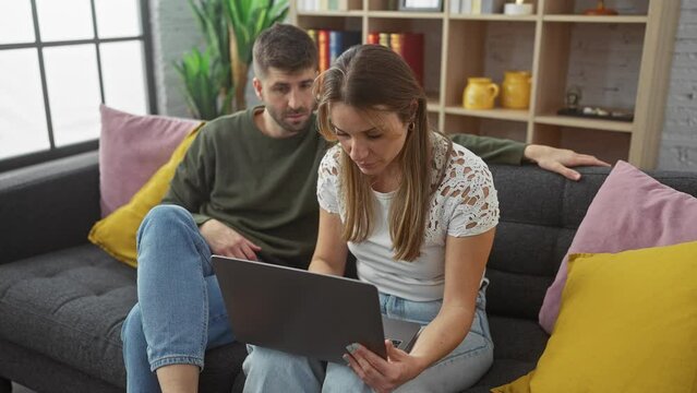 A woman and a man engaged in a high-five while using a laptop on a couch in a modern living room