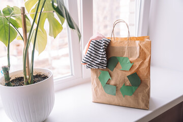 Paper bag with a recycling sign with old clothes on a windowsill with a flower.