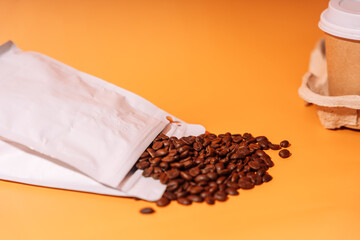 Paper cup in tray next to whole coffee beans on orange background.