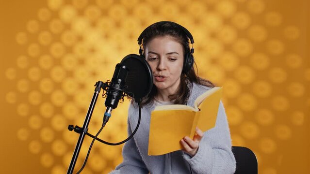 Woman does voiceover reading of book to produce audiobook using dramatic acting. Narrator uses storytelling skills and expressive sounds while producing recording of novel, studio background, camera B