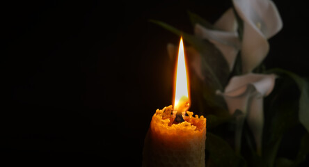White calla lily flowers and burning wax candle in darkness