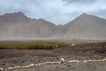Sand Storm in the cold desert of Nubra Valley in Ladakh, India. Background of Himalayas and dramatic clouds. View from a rocky road in the Himalayas. 