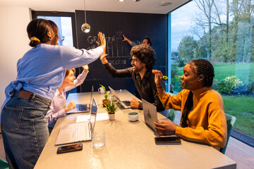 This vibrant image captures a multiracial team's celebratory moment inside a contemporary office. A man and woman engage in a high-five, signaling a shared success, as a colleague looks on with a