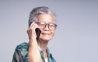 An elderly Asian woman with short white hair using a smartphone while standing on a gray background.