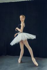 young ballerina in a tutu and pointe shoes standing against the wall posing ballet elements