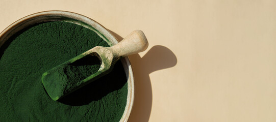 Natural organic green spirulina algae powder in bowl and wooden spoon on neutral background....