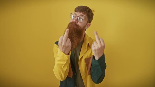 Cheeky young redhead guy in glasses and shirt, flashing a crude 'fuck off' sign, showing you his naughty, impolite attitude with a bad boy smirk over isolated yellow background.