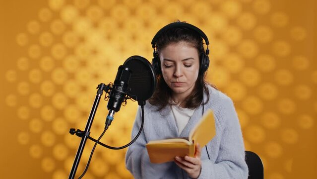 Lady browsing pages, doing voiceover reading of book to produce audiobook. Voice actor preparing to use storytelling skills to entertain audience while recording novel, studio background, camera B