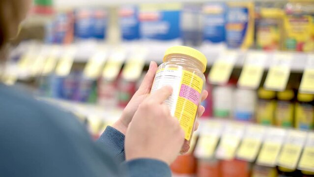 Close up of female hand holding vitamins, supplements,  read label information in drug store. Healthcare  concept