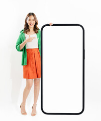 Cheerful and beautiful Asian woman stands beside a large smartphone mockup with a blank screen against a white background.