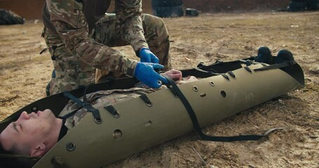 Close-up shot from the side of a confident young male military medic in army camouflage wearing blue medical gloves untying a special military green one worn to provide first aid to a wounded soldier