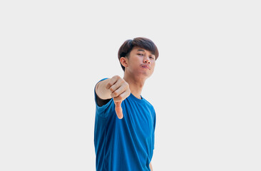 A young Asian man in his 20s wearing a blue t-shirt making a displeased gesture showing a thumbs down isolated on a gray background. The concept of expressing dislike or opposing opinions