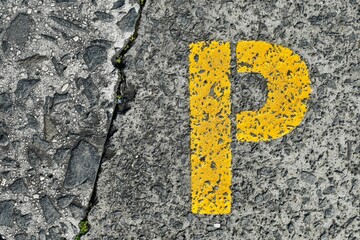 The letter P, in yellow, painted on a cement concrete road; for abstract background graphic design and a s asymbol of alphabet letters.
