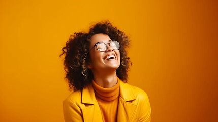 Happy woman wearing glasses, smiling warmly, arms crossed, against a bold mustard yellow backdrop, radiating joy