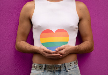 Unrecognizable homosexual man holding a rainbow heart in his hands isolated on purple background