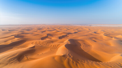 Fototapeta na wymiar Aerial view of a vast desert with sand dunes rippling towards the horizon under a clear blue sky