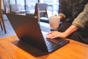 Closeup image of a woman working and touching on laptop computer touchpad while drinking coffee in...
