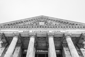The monochrome facade of the Reichstag building, showcasing its iconic pillars and inscription: Dem...
