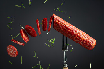 Traditional smoked salami sausage on a fork sprinkled with rosemary.