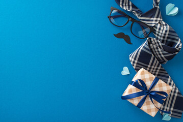 Celebration theme with top view of straw hat, stylish necktie, giftbox, glasses, mustache, hearts on blue backdrop. Ideal for Father's Day greetings or advert, featuring space for personalized message