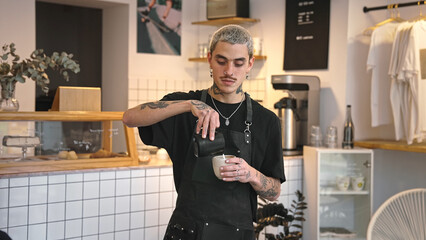 Handsome barista guy work coffee shop. Tattooed hipster man portrait. Happy male face smile. Joy young adult person look at camera cozy cafe house. Stylish dyed hair waiter make hot tasty drink order.