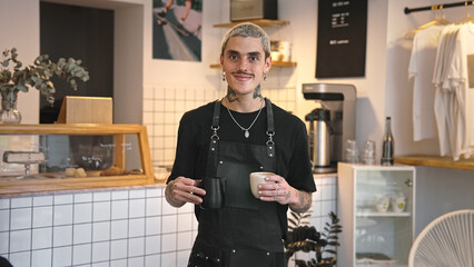 Handsome barista guy work coffee shop. Tattooed hipster man portrait. Happy male face smile. Joy young adult person look at camera cozy cafe house. Stylish dyed hair waiter make hot tasty drink order.