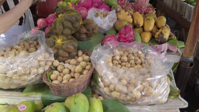 An Asian lady purchases a variety of tropical fruits langsat, duku, salak, mango, apple, orange dragon fruits at the asian wet traditional fruit market in indonesia.