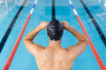 Caucasian young male swimmer adjusting swim cap at pool indoors