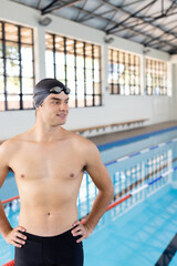 Caucasian young male swimmer standing by pool indoors, looking away