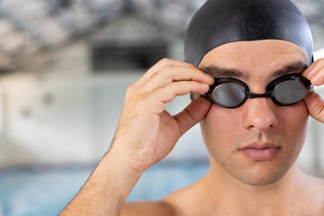 Caucasian young male swimmer adjusting goggles indoors, standing by pool, copy space