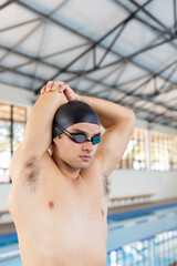 Caucasian young male swimmer stretching before training indoors in pool