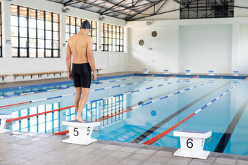 Caucasian young male swimmer standing on starting block at pool indoors, copy space