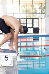 Caucasian young male swimmer preparing to dive into an indoor pool, copy space
