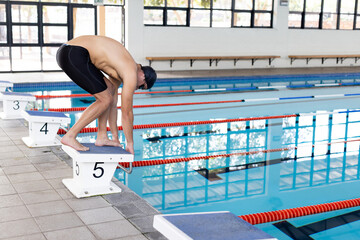 Caucasian young male swimmer preparing to dive into an indoor pool