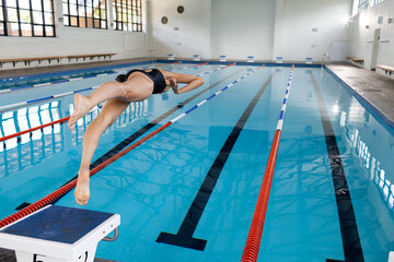 A biracial young female swimmer diving into indoor swimming pool, copy space