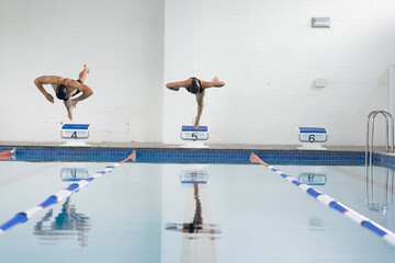 Diverse young swimmers diving into indoor swimming pool, copy space