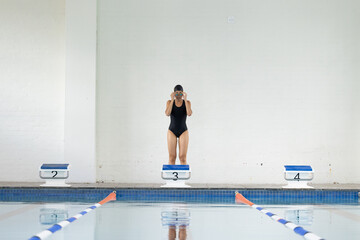 A biracial young female swimmer in black swimsuit preparing to dive indoors