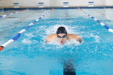 Caucasian young male swimmer training indoors in swimming pool, wearing goggles