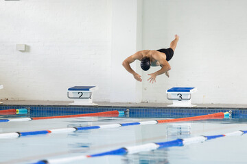 Caucasian young male swimmer diving into indoor swimming pool, wearing black cap, copy space