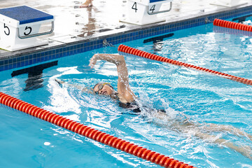 A biracial young female swimmer wearing goggles, training in indoor swimming pool - Powered by Adobe